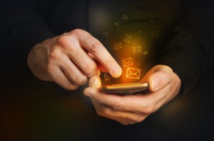 Man in black shirt is typing a text message on his smartphone, close up image, focus on hands and the phone device.